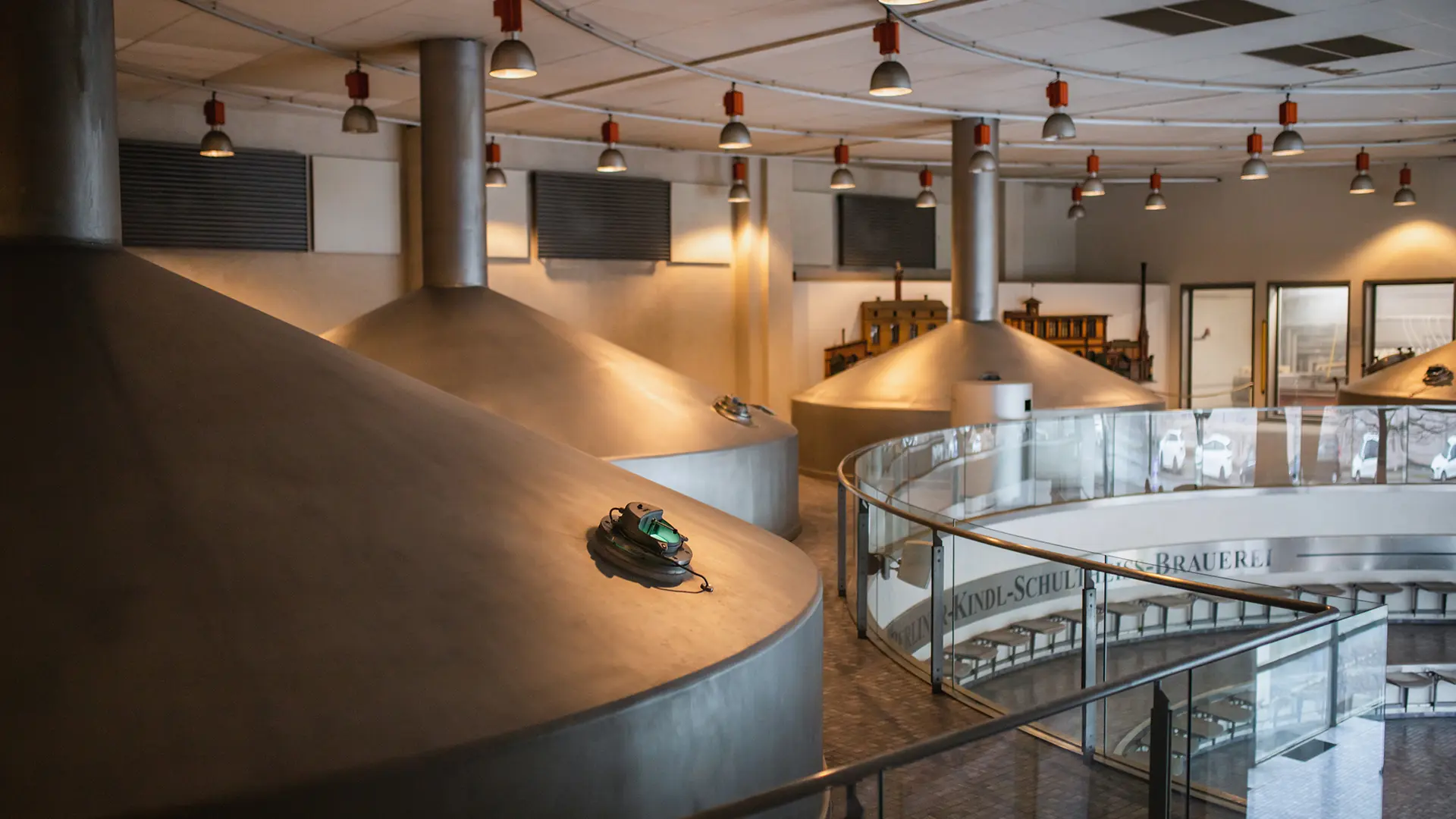 Große Braukessel aus Metall stehen in einer Brauerei mit Beleuchtung an der Decke.