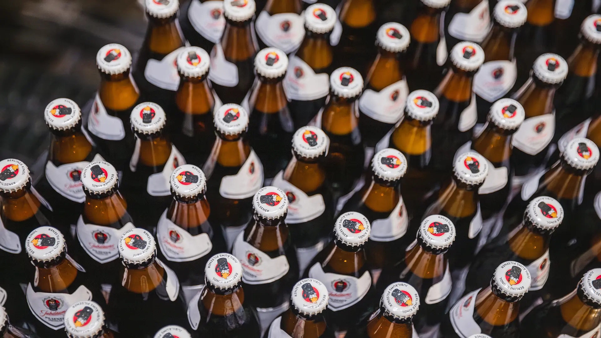 Viele Bierflaschen sind eng aneinander gereiht, jede mit einem roten Verschluss.
