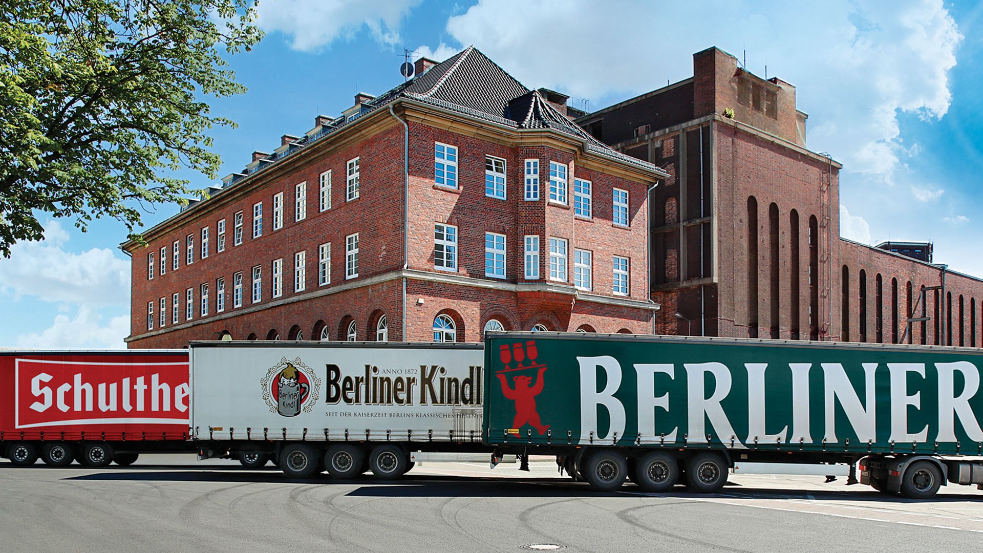 Zwei Lkw fahren vor einem historischen Ziegelgebäude entlang einer Straße.