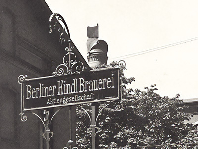 Schmiedeeisernes Schild einer Brauerei mit dekorativen Elementen hängt an einer Hauswand.