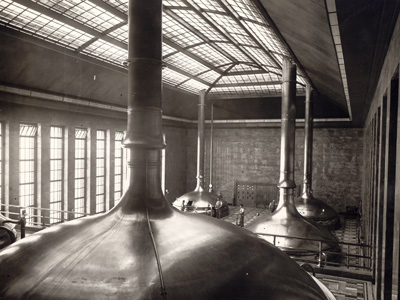Große Kupferkessel stehen in einer Industriehalle mit vielen Fenstern.