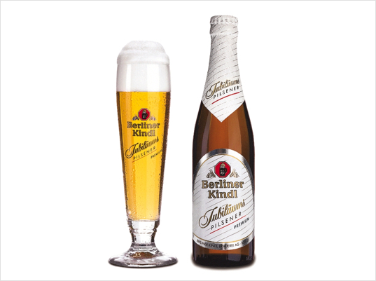Ein volles Bierglas steht neben einer ungeöffneten Bierflasche auf weißem Hintergrund.