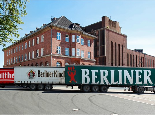 Ein großer LKW fährt vor einem roten Backsteingebäude entlang.