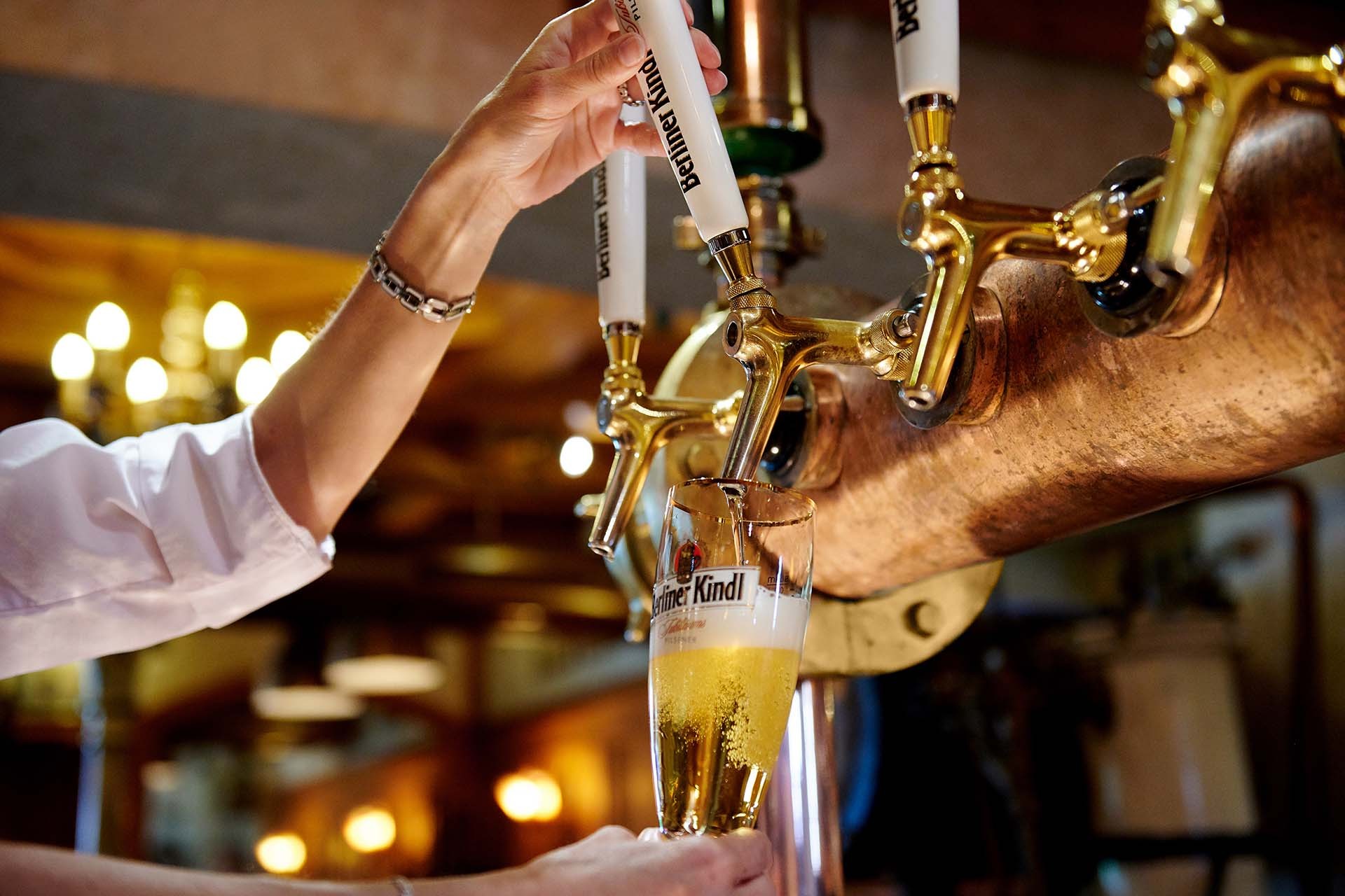 Eine Person zapft Bier aus einem goldenen Zapfhahn in ein hohes Glas.