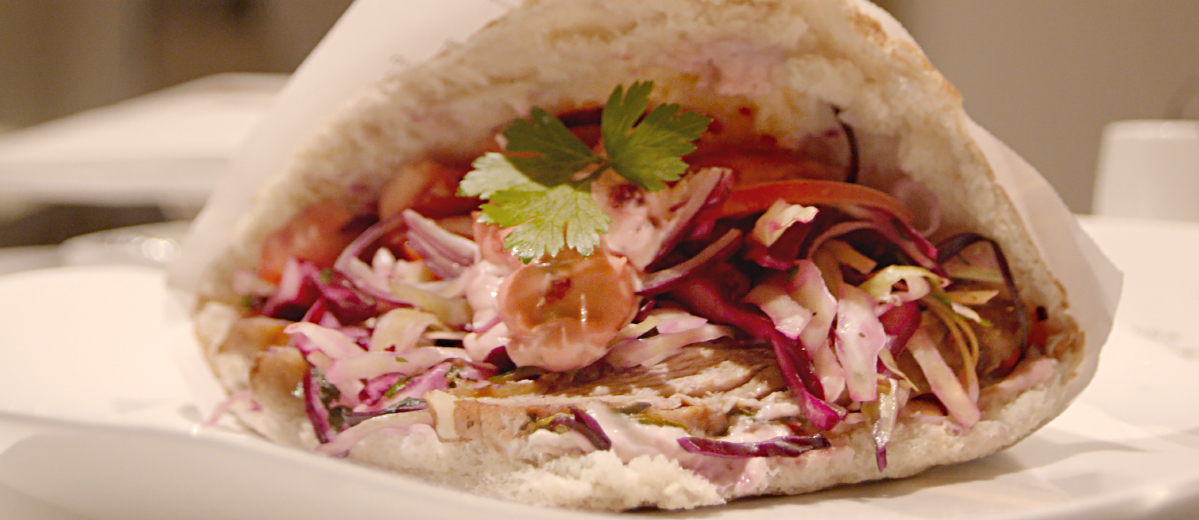 Ein gefülltes Fladenbrot liegt auf einem weißen Teller, garniert mit Rotkohl und Petersilie.