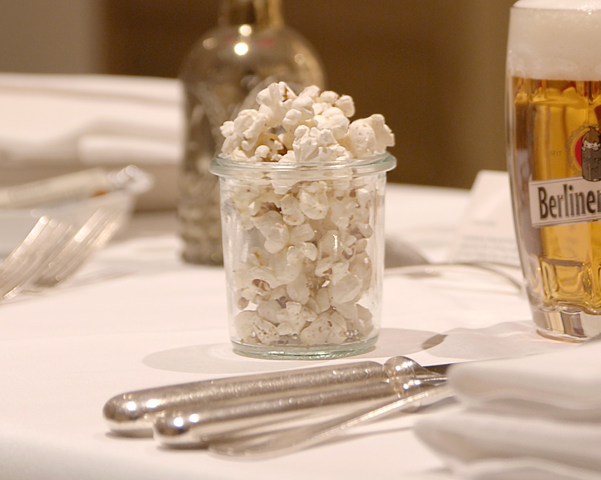 Ein Glas mit Popcorn steht auf einem gedeckten Tisch neben einem Bierglas.