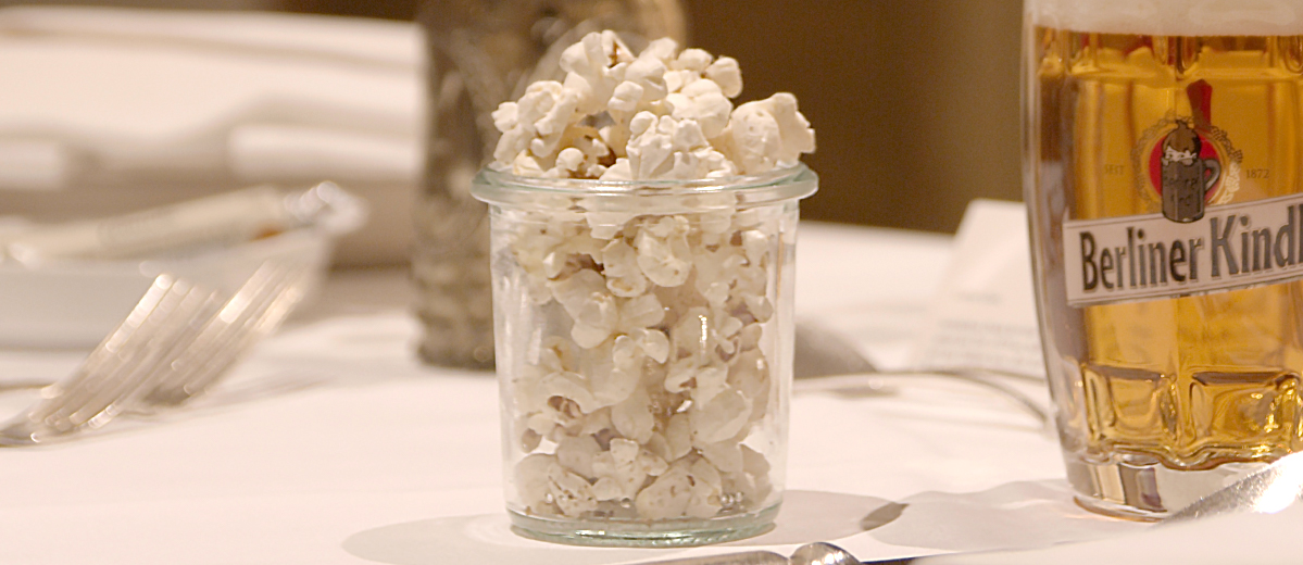 Ein Glas mit Popcorn steht auf einem gedeckten Tisch neben einem Bierglas.