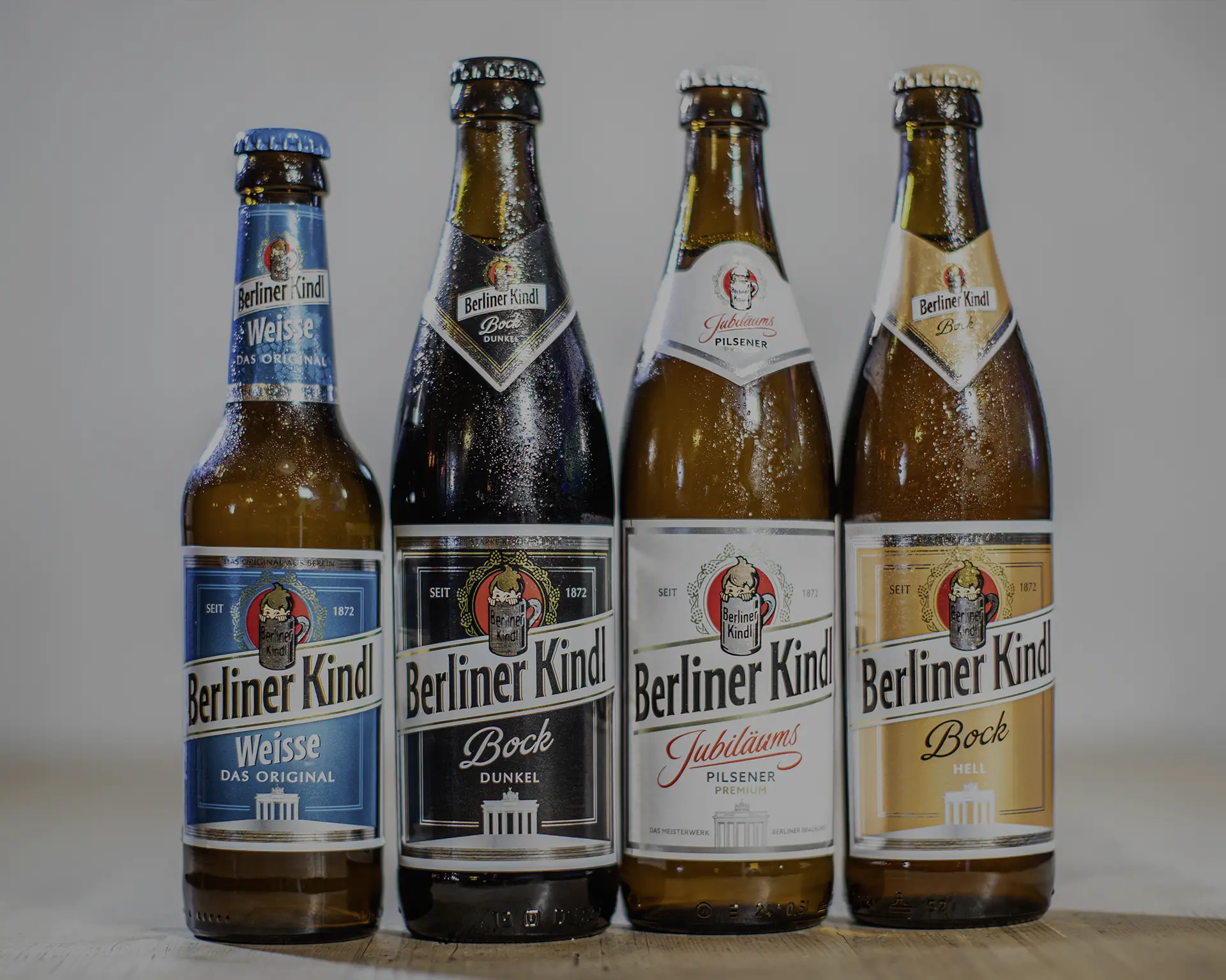 Vier Flaschen Bier stehen auf einem rustikalen Holztisch. Jede besitzt unterschiedliche Etiketten.