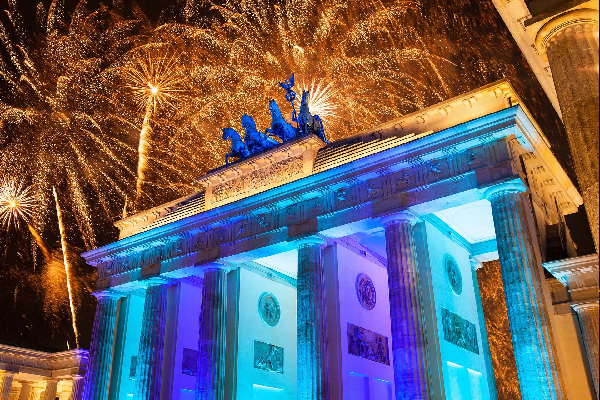 Beleuchtetes Tor mit Statue oben und Feuerwerk im Hintergrund. Die Struktur erscheint in Blau mit goldenen Lichtexplosionen.