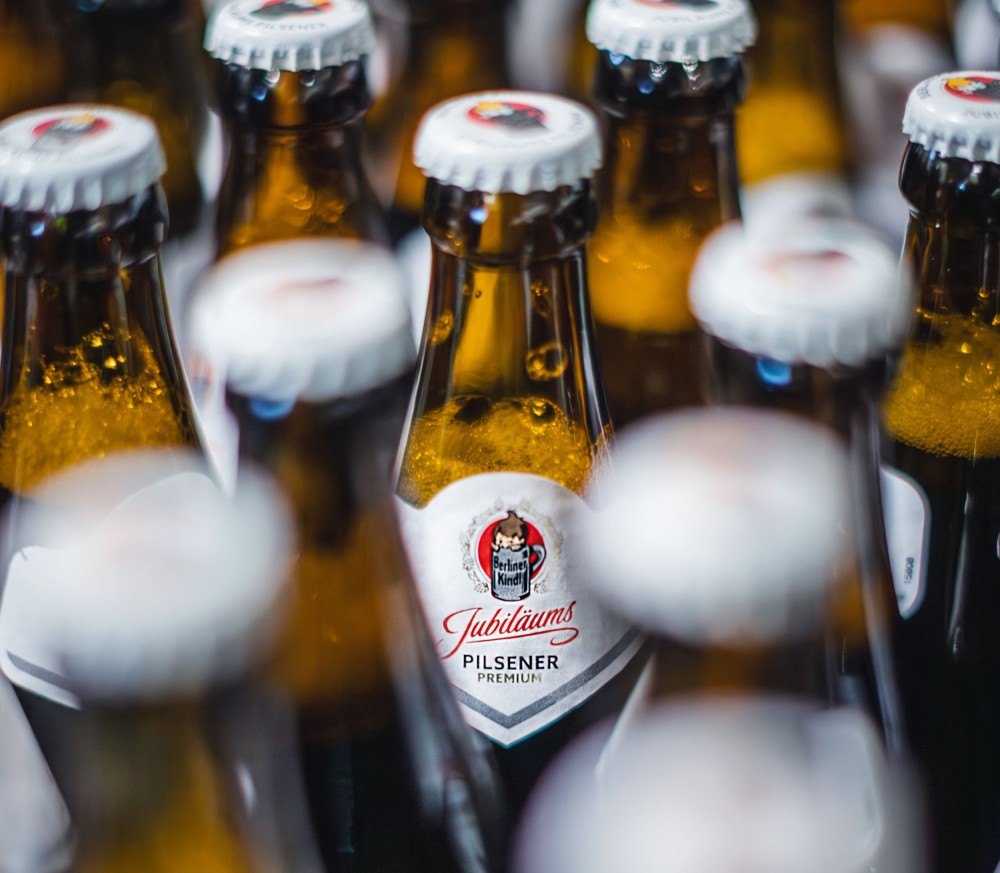 Szene in einer Bar, zwei Berliner Kindl Bierflaschen im Vordergrund beim Anstoßen.